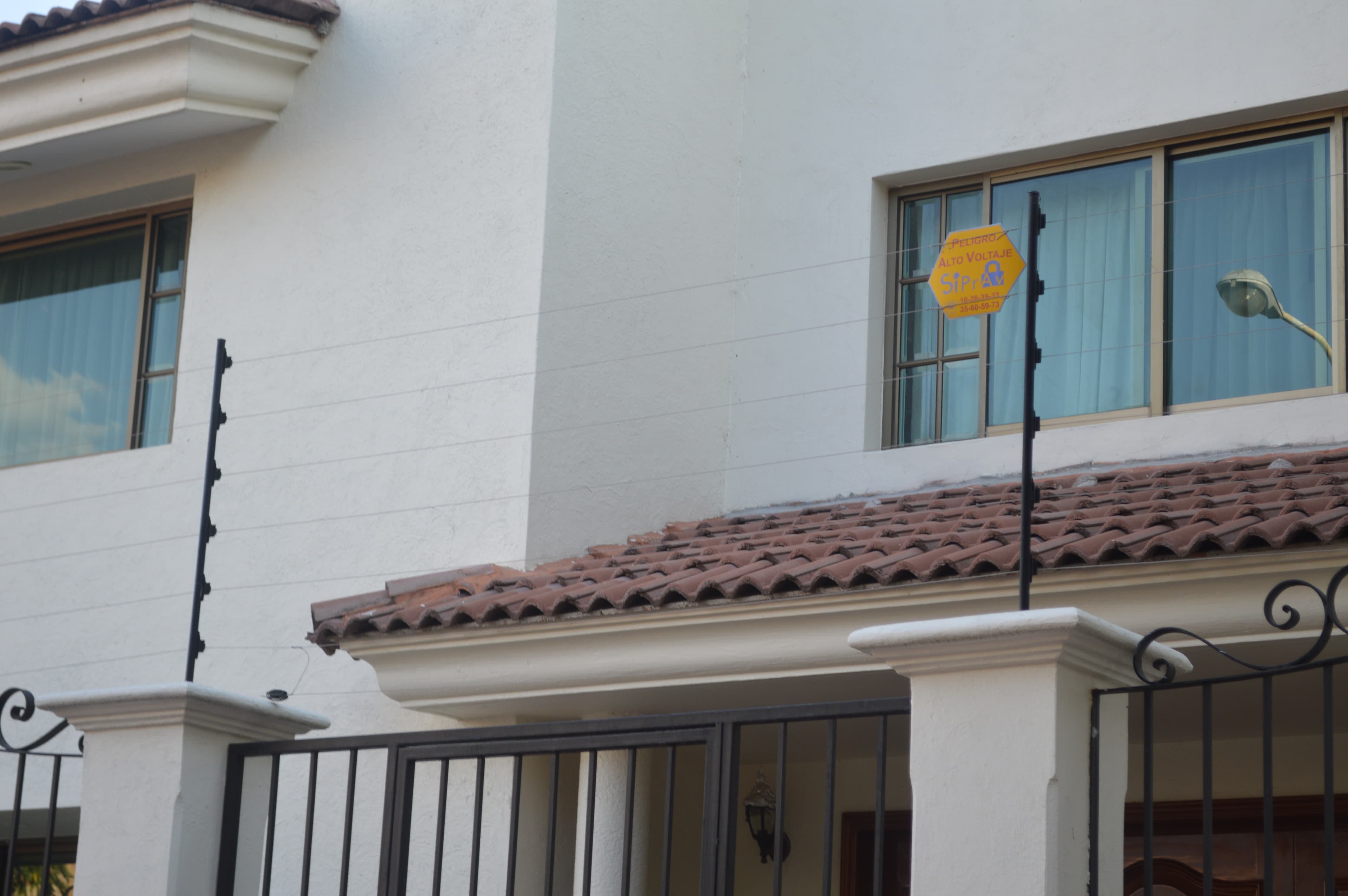 Cerca eléctrica de seguridad montada sobre una barda residencial, con letrero de peligro visible