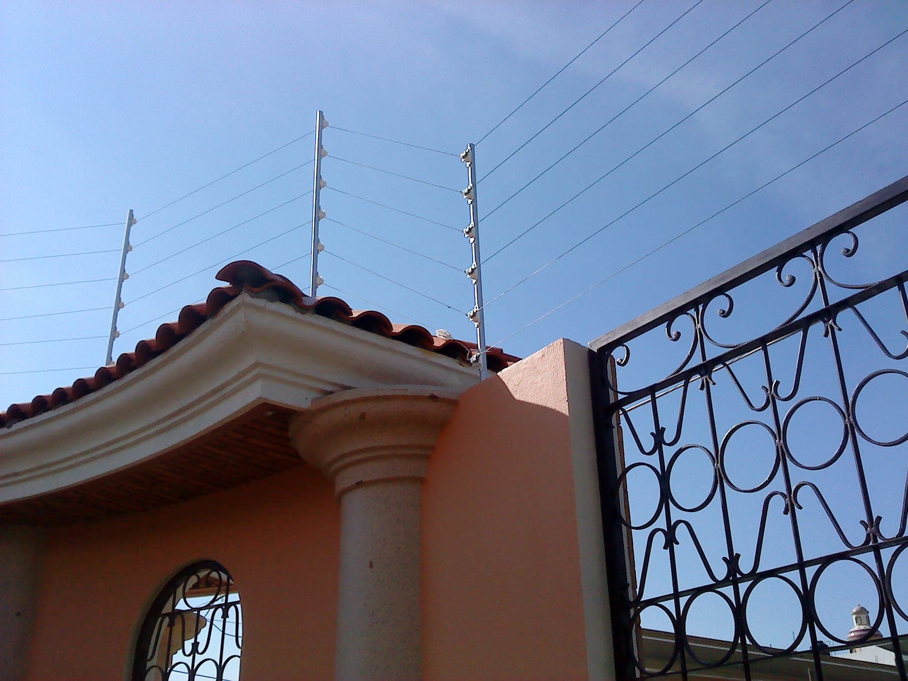 Cerca eléctrica sobre la barda de una casa de estilo colonial con cúpula y portón de herrería