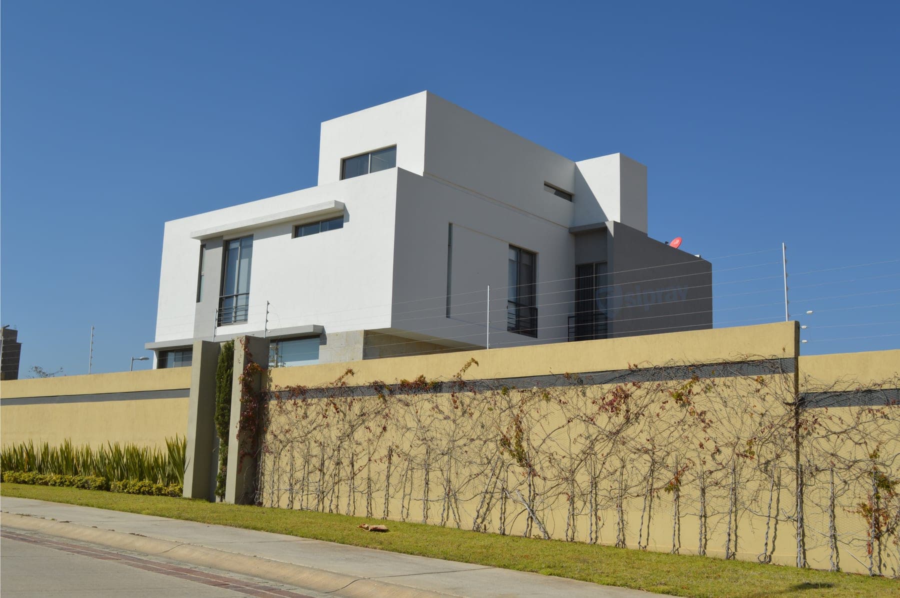 Cerca eléctrica sobre barda con enredadera, frente a una casa contemporánea blanca