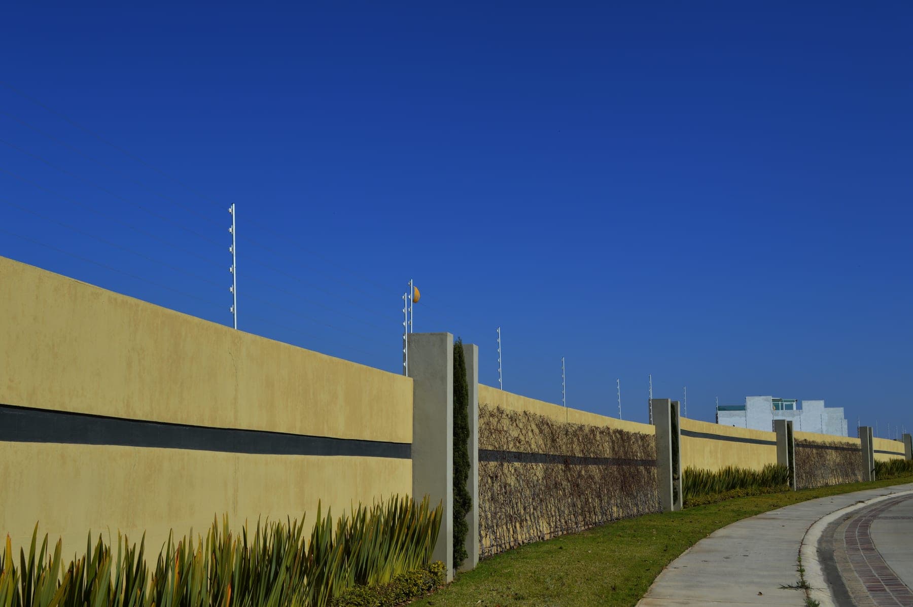 Cerca eléctrica a lo largo de una barda extensa con jardinera y banqueta