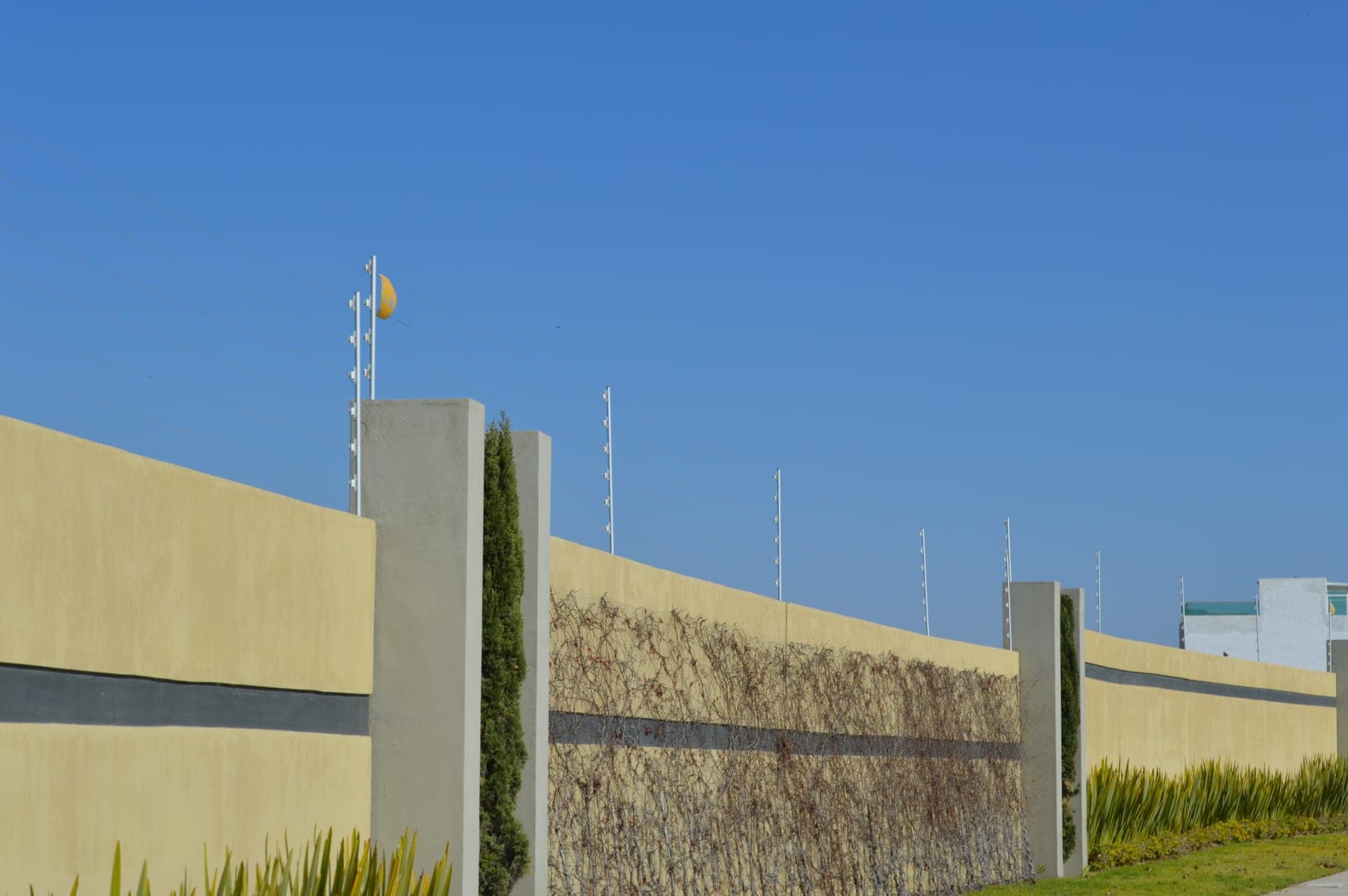 Postes blancos de cerca eléctrica alineados con las pilastras de una barda larga