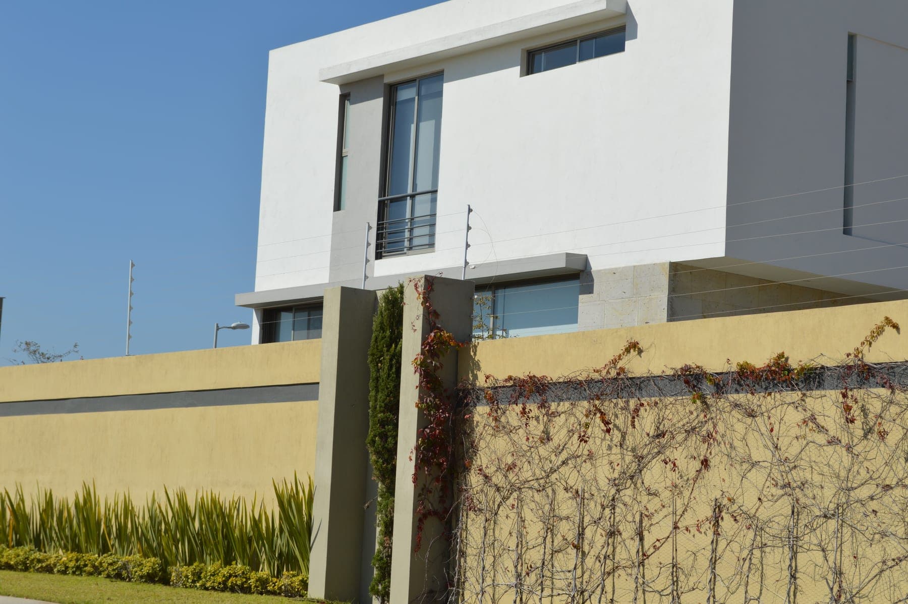 Cerca eléctrica sobre barda con enredadera frente a una casa blanca de dos niveles