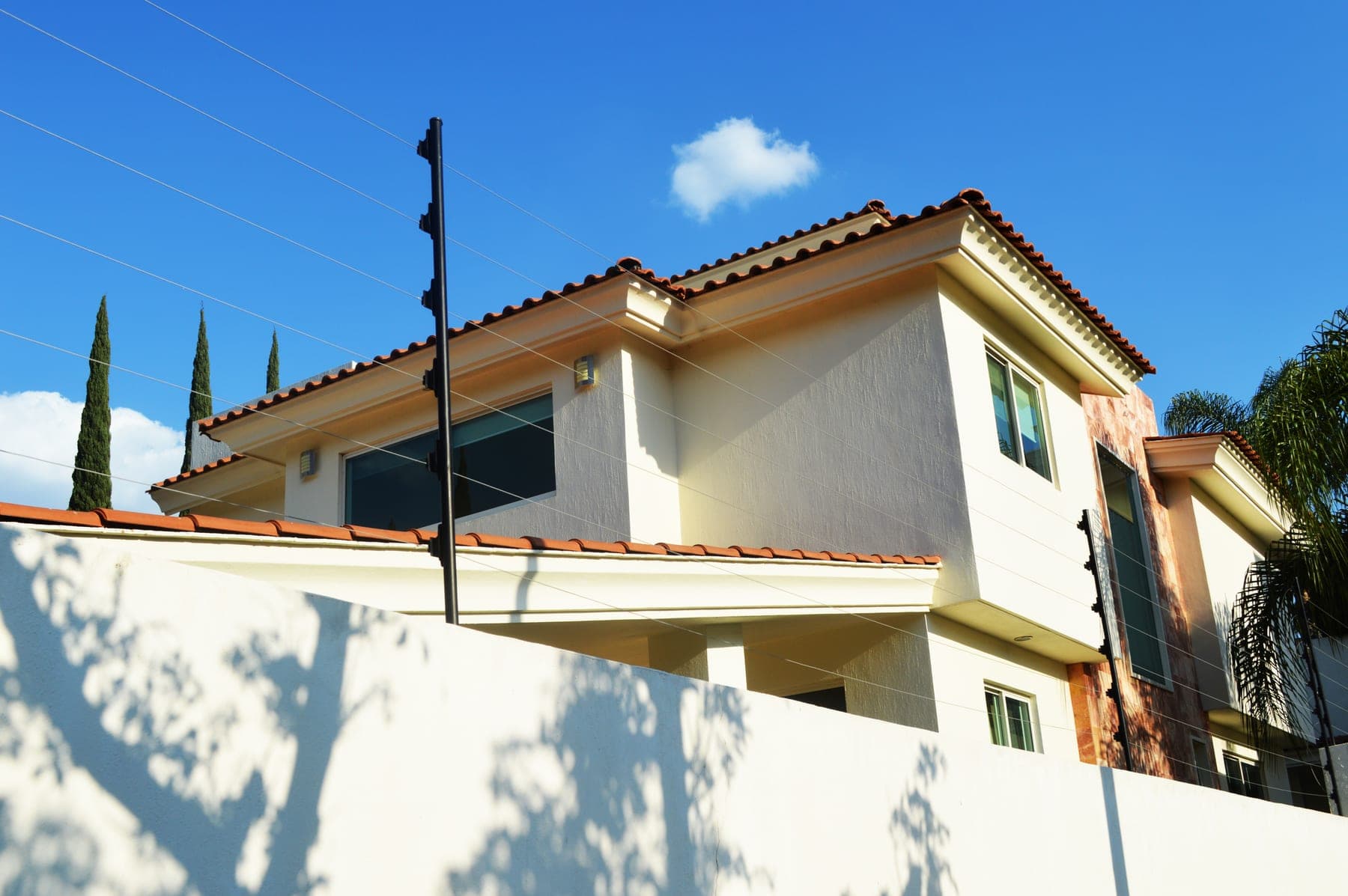 Cerca eléctrica de postes negros montada sobre la barda de una residencia de teja