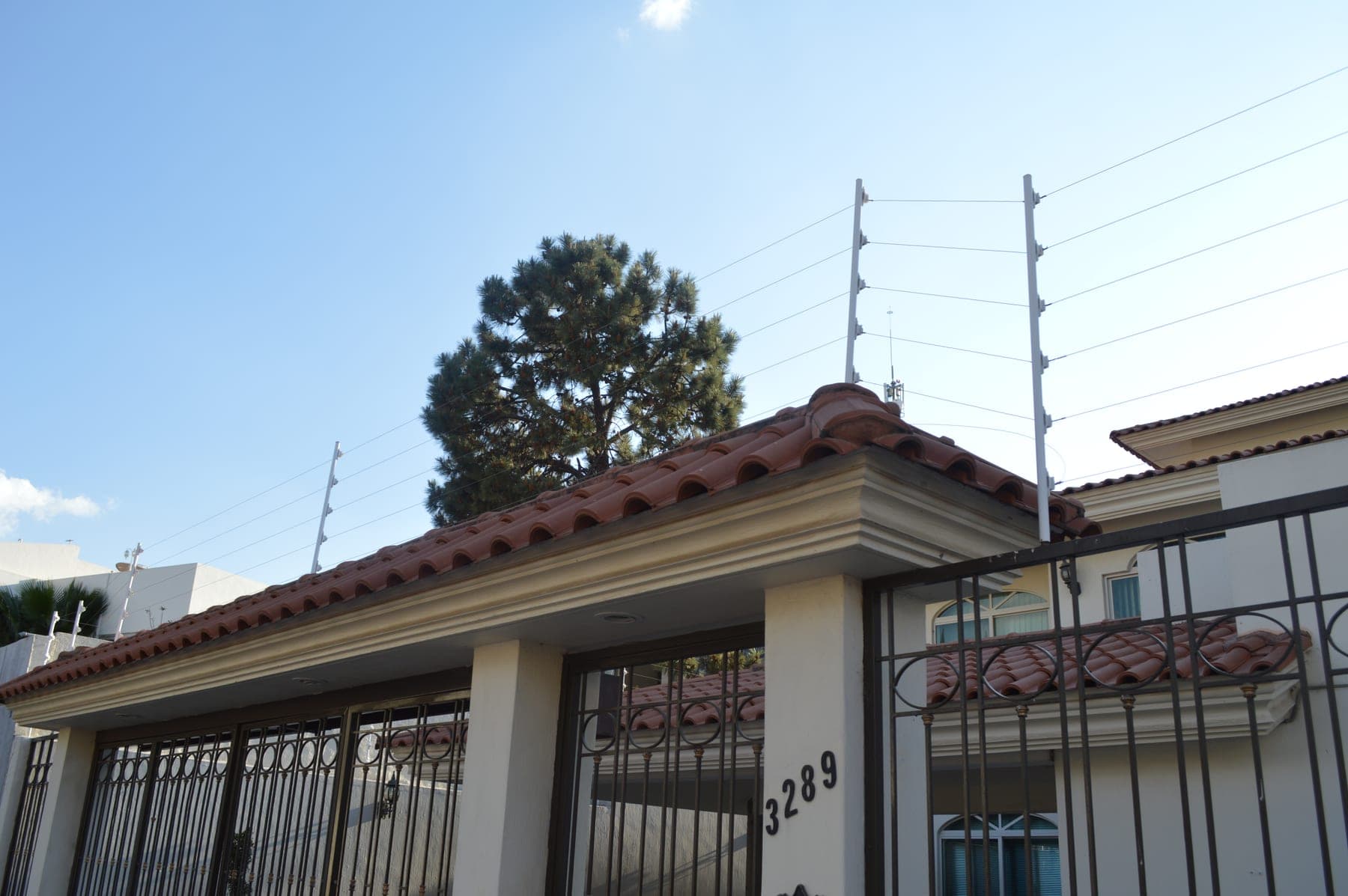 Cerca eléctrica sobre una residencia con columnas y portón de herrería