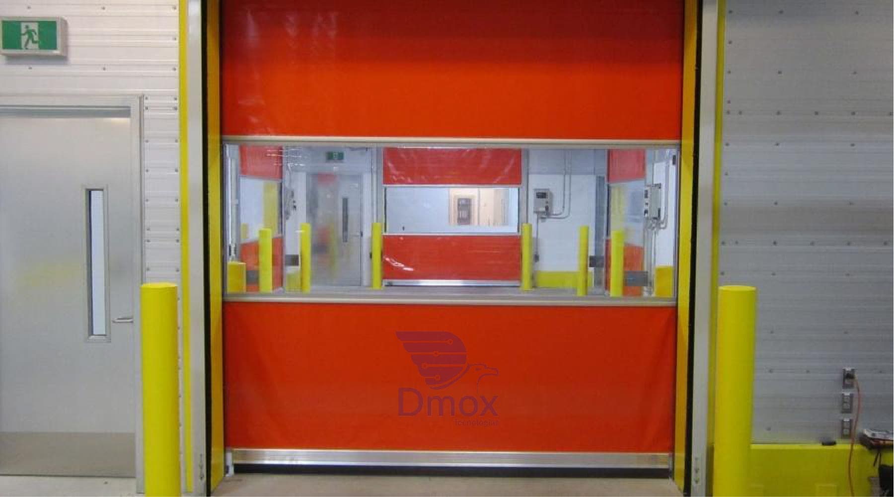 Puerta rápida naranja con ventana panorámica y postes amarillos de protección en un pasillo interior