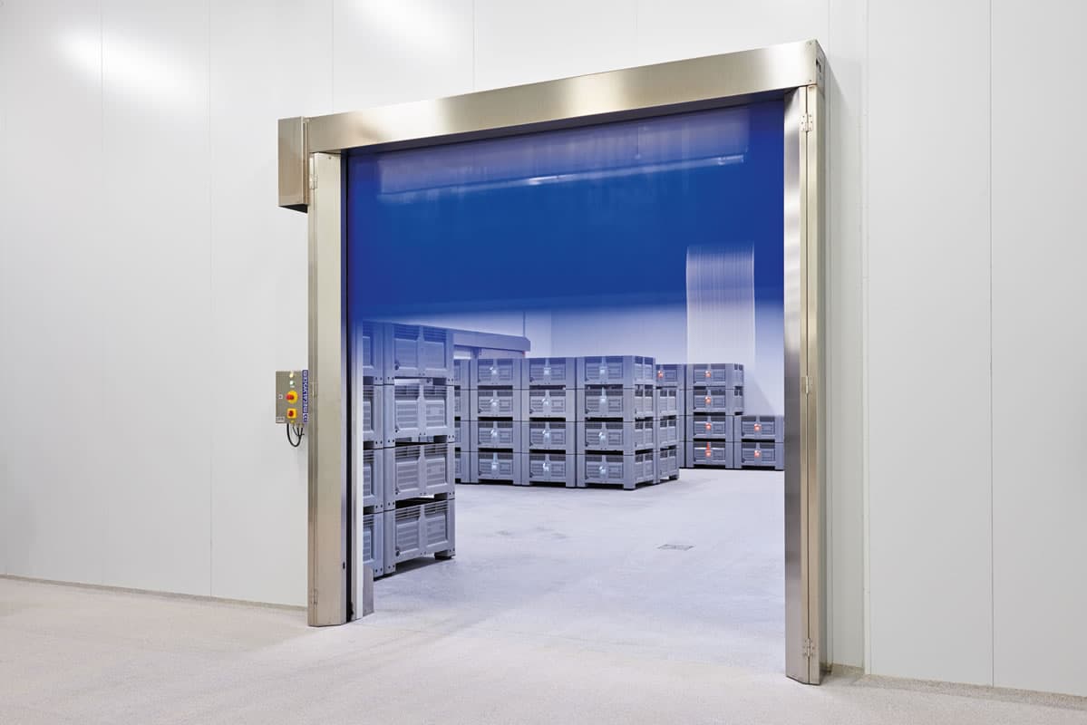 Puerta rápida industrial enrollable de PVC azul a medio abrir, con bastidor de acero inoxidable, separando un área de almacenamiento refrigerado